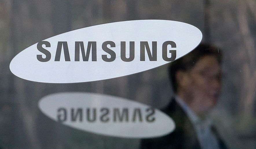 FILE - In this April 6, 2018, file photo, an employee walks past logos of the Samsung Electronics Co. at its office in Seoul, South Korea. Samsung Electronics says it will spend $22 billion over the next three years on artificial intelligence, auto components, and other future businesses. (AP Photo/Ahn Young-joon, File)