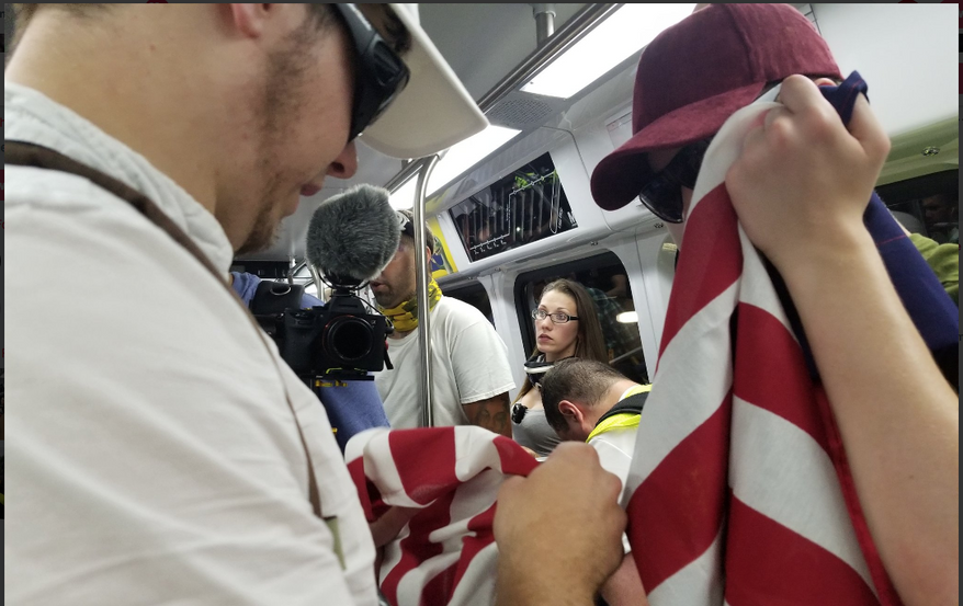 Attendees for a white nationalist rally in Washington, D.C., hold an American flag as they travel via a subway train from Vienna, Virginia, on Sunday. As many as 400 people were permitted to rally in the "Unite the Right 2" event marking the one-year anniversary of a violent gathering in Charlottesville, Virginia. Photo by Julia Airey / The Washington Times