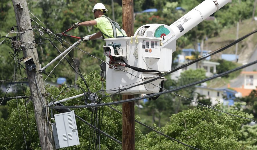 FILE- In this May 16, 2018 file photo, a worker from the Cobra Energy Company, contracted by the Army Corps of Engineers, installs power lines in the Barrio Martorel area of Yabucoa, Puerto Rico. Officials said on Tuesday, Aug. 14, that the power has been restored to the entire island for the first time since Hurricane Maria struck nearly 11 months ago. (AP Photo/Carlos Giusti, File)