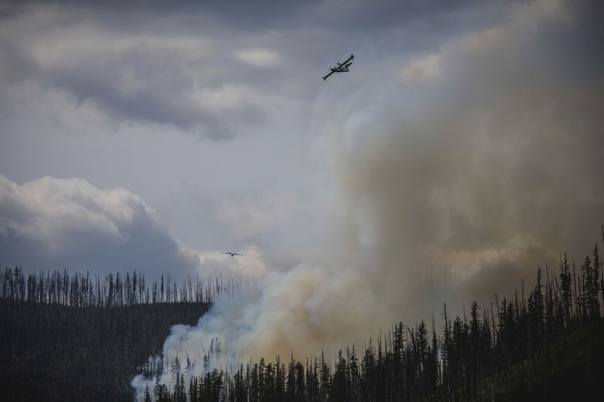 In this Sunday, Aug. 12, 2018 photo provided by the National Park Service, a Canadian CL-215 "superscooper" airplane drops water on the Howe Ridge Fire in Glacier National Park, Mont. A wildfire destroyed structures and forced evacuations Monday from the busiest area of Montana's Glacier National Park, as officials in California prepared to reopen Yosemite National Park Tuesday following a nearly three-week closure at the height of the summer season. (National Park Service via AP)