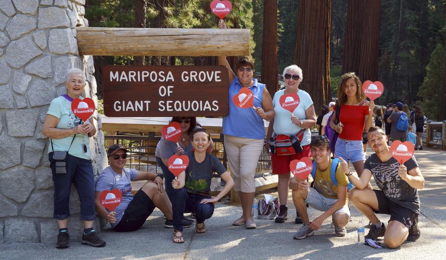 This photo provided by Visit Yosemite, Madera County Visitors Bureau, shows Yosemite National Park employees, and a few visitors from France, posing for a photo holding hand fans that read #YosemiteNOW, a hashtag being used to spread the word that the park is open, at the park&#x27;s Mariposa Grove of Giant Sequoias Monday, Aug. 13, 2018. Most of Yosemite is set to reopen Tuesday, Aug. 14, 2018 after a 20-day closure, resulted from a wildfire. (Steve Montalto/Visit Yosemite, Madera County Visitors Bureau via AP)
