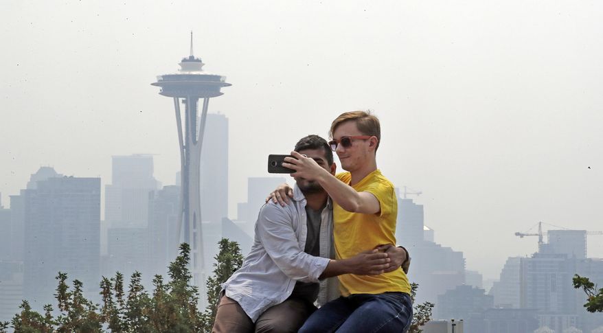 Adi Kang, left, and Brendon Walter take a photo together as a smoky haze obscures the Space Needle and downtown Seattle behind them, Tuesday, Aug. 14, 2018. Public-health officials are warning of unhealthy air across parts of the Pacific Northwest as smoke from wildfires move across the region. (AP Photo/Elaine Thompson)