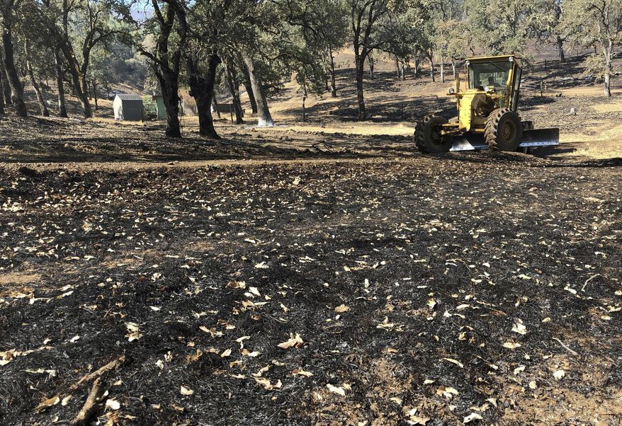 In this Friday, Aug. 10, 2018 photo, Jack Hattendorf steers a road grader to repair a dirt path near Lakeport, Calif. Even as flames continue chewing through forestland nearby, Hattendorf and others are working to repair the damage wrought not by flames but by firefighters trying to stop them. (AP Photo/Jonathan J. Cooper)