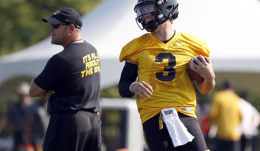 File-This Aug. 3, 2018, file photo shows Missouri quarterback Drew Lock, right, smiling as he runs past head coach Barry Odom during an NCAA college football practice in Columbia, Mo. When former Missouri offensive coordinator Josh Heupel left to become the head coach at Central Florida last year, it meant that Lock would play his senior season with a third offensive coordinator in four years. (AP Photo/Jeff Roberson, File)