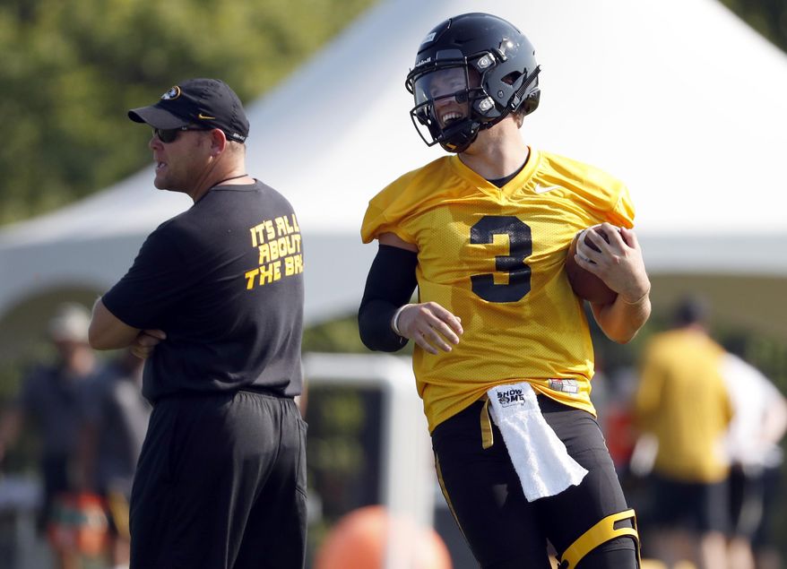 File-This Aug. 3, 2018, file photo shows Missouri quarterback Drew Lock, right, smiling as he runs past head coach Barry Odom during an NCAA college football practice in Columbia, Mo. When former Missouri offensive coordinator Josh Heupel left to become the head coach at Central Florida last year, it meant that Lock would play his senior season with a third offensive coordinator in four years. (AP Photo/Jeff Roberson, File)