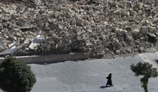 In this photo taken on Thursday, Aug. 16, 2018, a woman walks past the remnants of destroyed buildings in the city of Aleppo, Syria. Russian air defense assets in Syria claim to have downed 45 drones targeting their main base in the country, its military said Thursday, after an attack by the Islamic State group on a Syrian army base a day earlier killed seven troops. (AP Photo/Sergei Grits)