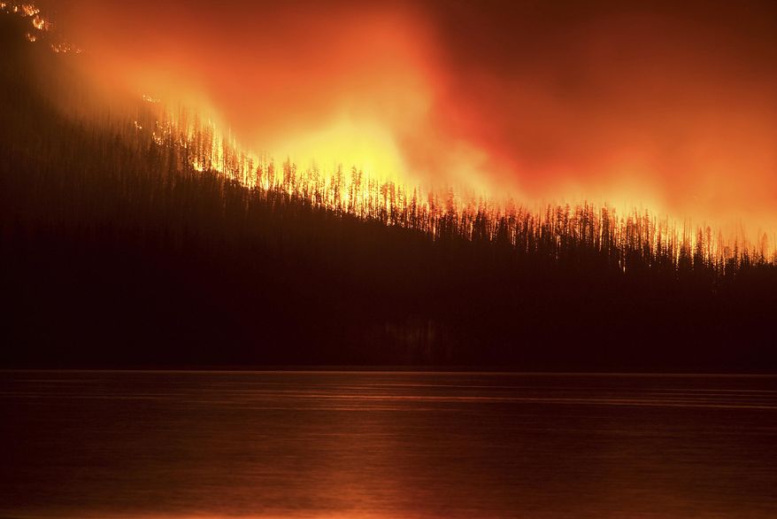 FILE--In this file photo taken Aug. 12, 2018, a fire burns next to Lake McDonald in Glacier National Park in northwest Montana. It's a good news, bad news situation for firefighters working in Glacier National Park. While the forecast calls for cooler weather and higher humidity, gusting winds and thunderstorms also are predicted. (Chris Peterson/Hungry Horse News via AP, file)