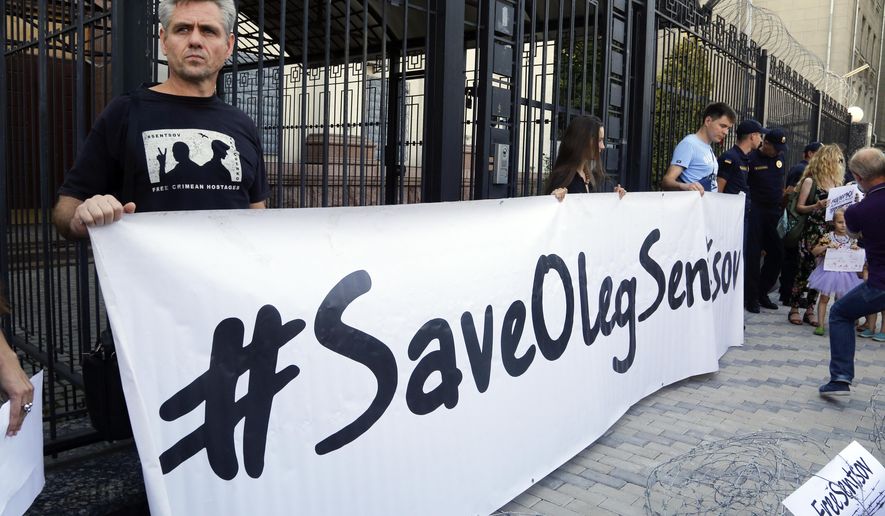 People hold posters to support Ukrainian filmmaker Oleg Sentsov, who is currently on hunger strike in a Russian jail to demand the release of the other Ukrainian hostages taken by the Kremlin, in front of the Embassy of the Russian Federation in Kiev, Ukraine, Tuesday, Aug. 21, 2018. Today is the 100th day since the beginning of the indefinite hunger strike of Oleg Sentsov, announced on May 14, 2018, demanding the release of all Ukrainian political prisoners of the Kremlin. (AP Photo/Efrem Lukatsky)