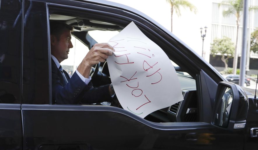 U.S. Rep. Duncan Hunter holds a sign that reads &amp;quot;lock him up!&amp;quot;, that was placed on the windshield of his car by a protester, as he leaves an arraignment Thursday, Aug. 23, 2018, in San Diego. Hunter and his wife Margaret pleaded not guilty Thursday to charges they illegally used his campaign account for personal expenses. (AP Photo/Gregory Bull)