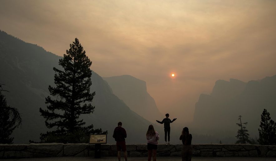 FILE - In this July 25, 2018 file photo, Hannah Whyatt poses for a friend's photo as smoke from the Ferguson fire fills Yosemite Valley in Yosemite National Park, Calif. Alarmed by as much as $20 million in lost tourism revenue in July due to visitors' fear of wildfires, California tourism officials are teaming up with Oregon and Washington to reassure tourists they're safe to visit after deadly wildfires that have burned homes and clogged the air. (AP Photo/Noah Berger, File)