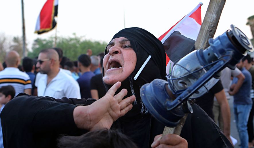 A woman holds an oil lamp while chant slogans demanding better public services and jobs during a protest in front of the provincial council building in Basra, 340 miles (550 km) southeast of Baghdad, Iraq, Friday, Aug. 10, 2018. (AP Photo/Nabil al-Jurani)