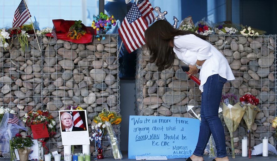 Thu-Van Cunningham, of Phoenix, reads messages left by well-wishers as she visits a makeshift memorial in honor of the late Arizona Republican Sen. John McCain at McCain's office Monday, Aug. 27, 2018, in Phoenix. McCain, the war hero who became the GOP's standard-bearer in the 2008 election, died at the age of 81, Saturday, Aug. 25, 2018, after battling brain cancer. (AP Photo/Ross D. Franklin)