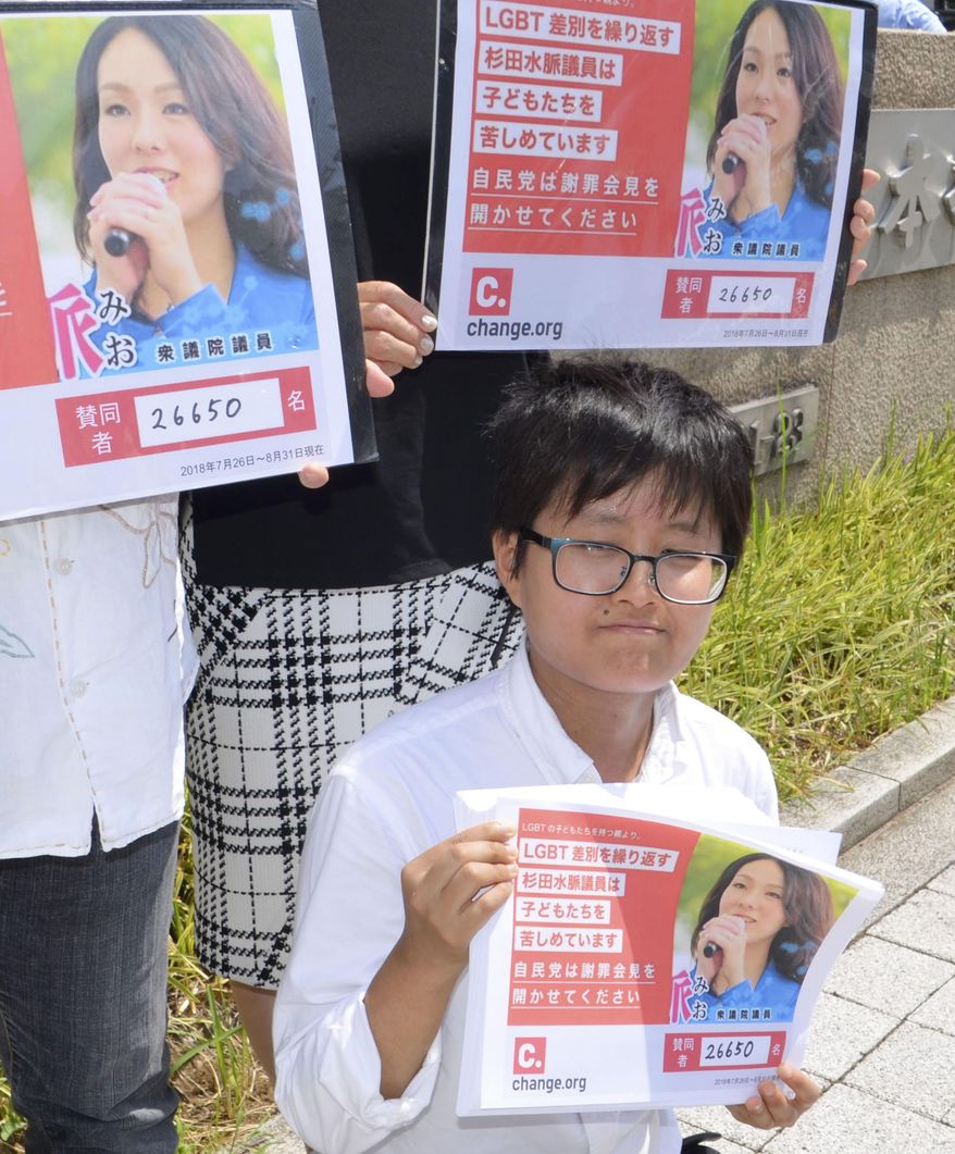 Activist Mameta Endo, bottom, poses with about 26,000 signatures to submit to Liberal Democratic Party requesting that lawmaker Mio Sugita hold a press conference to apologize in front of ruling Liberal Democratic Party headquarters Friday, Aug. 31, 2018 in Tokyo. Japanese activists including seven parents of LGBT children have submitted the petition to Prime Minister Shinzo Abe’s party, demanding that the lawmaker apologize for saying that sexual minorities are unproductive and don’t deserve public support. (Kyodo News via AP)