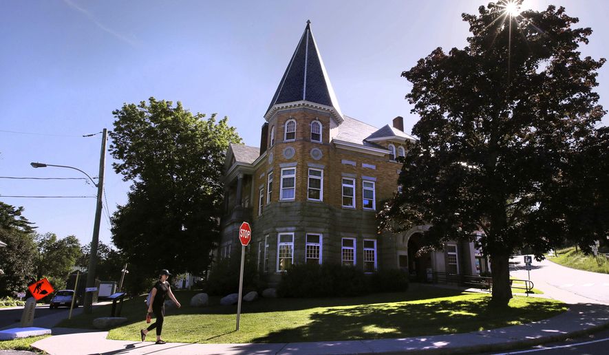 FILE - In this July 11, 2018 file photo, a library patron freely crosses the United States border from Quebec into Vermont as she walks down the sidewalk during a visit to the Haskell Library, rear, in Derby Line, Vt. A Montreal man is due in a Burlington court for sentencing after he pleaded guilty to charges he helped smuggle more than 100 handguns from the United States to Canada, some through the Haskell Library. (AP Photo/Charles Krupa, File)