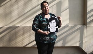 In this Thursday, Sept. 6, 2018 photo, 54-year-old teacher Vittoria E Natto poses for a portrait inside her high school holding a photo of herself when she was 9 years old, in Santiago, Chile. Forty-five years after the Chilean coup led by Gen. Augusto Pinochet, there are still stories to tell of the horrors that followed the Sept. 11, 1973, overthrow of President Salvador Allende. That repression is still stamped on the mind of Natto, who uses a pseudonym to write and speak about her history. (AP Photo/Esteban Felix)