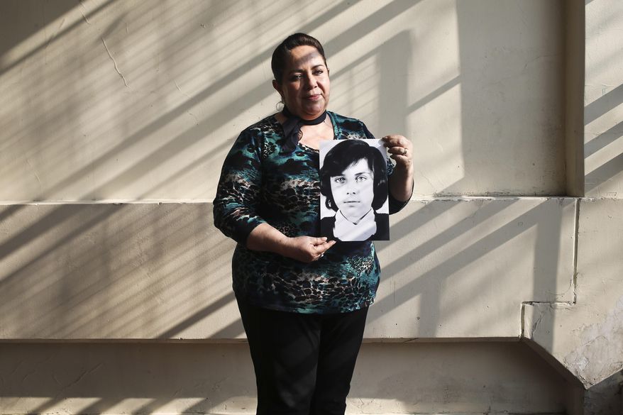 In this Thursday, Sept. 6, 2018 photo, 54-year-old teacher Vittoria E Natto poses for a portrait inside her high school holding a photo of herself when she was 9 years old, in Santiago, Chile. Forty-five years after the Chilean coup led by Gen. Augusto Pinochet, there are still stories to tell of the horrors that followed the Sept. 11, 1973, overthrow of President Salvador Allende. That repression is still stamped on the mind of Natto, who uses a pseudonym to write and speak about her history. (AP Photo/Esteban Felix)
