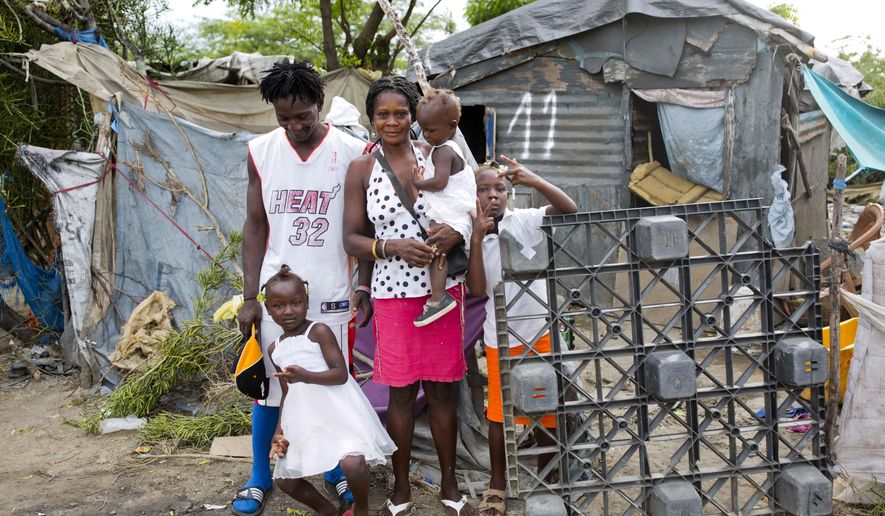 In this Aug. 29, 2018 photo, Changlair Aristide stands with his wife Violene Mareus and children outside their home near the Truitier landfill where Aristide scavenges for valuables to use or sell in the Cite Soleil slum of Port-au-Prince, Haiti, before Aristide leaves to play soccer with a group of friends. Mareus said she hopes to move to a nice home one day in which she doesn't have to hold up tarps when it rains. (AP Photo/Dieu Nalio Chery)