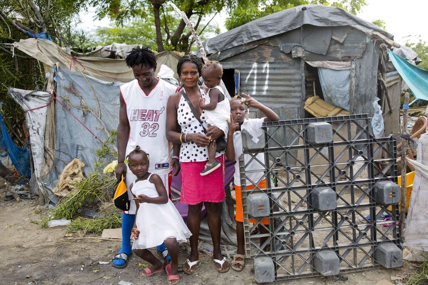 In this Aug. 29, 2018 photo, Changlair Aristide stands with his wife Violene Mareus and children outside their home near the Truitier landfill where Aristide scavenges for valuables to use or sell in the Cite Soleil slum of Port-au-Prince, Haiti, before Aristide leaves to play soccer with a group of friends. Mareus said she hopes to move to a nice home one day in which she doesn't have to hold up tarps when it rains. (AP Photo/Dieu Nalio Chery)