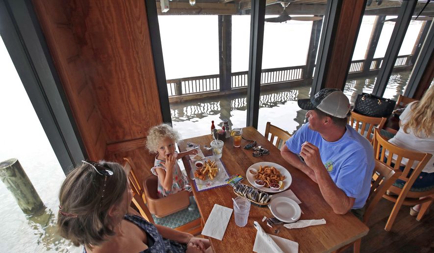 Blythe Hayes, left, with her daughter Erin Hayes, 3, and her husband Sean Hayes, from Manteo, N.C., eats at Bubba's Seafood Restaurant even though the deck has a few inches of water on it, Friday, Sept. 14, 2018, in Virginia Beach, Va., as the effects of Hurricane Florence are felt in the area. (AP Photo/Alex Brandon)