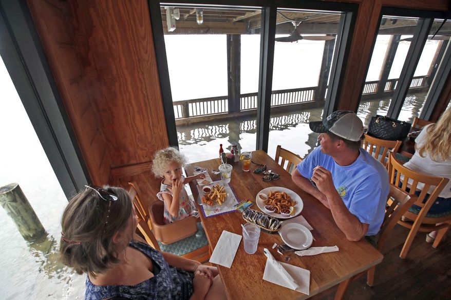 Blythe Hayes, left, with her daughter Erin Hayes, 3, and her husband Sean Hayes, from Manteo, N.C., eats at Bubba's Seafood Restaurant even though the deck has a few inches of water on it, Friday, Sept. 14, 2018, in Virginia Beach, Va., as the effects of Hurricane Florence are felt in the area. (AP Photo/Alex Brandon)