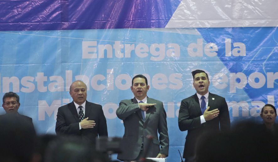 Guatemalan President Jimmy Morales, center, sings the national anthem, acompanied by Mixco mayor Ernesto Bran, right, and Culture Minister Jose Chex, during the inauguration of a soccer field in Mixco, Guatemala, Monday, Sept. 17, 2018. Morales' government will defy a ruling by the country's top court and block the return of Ivan Velasquez, who is leading a U.N.-backed anti-corruption commission. (AP Photo/Moises Castillo)