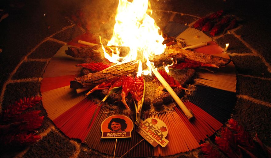 A small sign with a picture of murdered environmental activist Berta Caceres reads in Spanish, "We demand judgment and punishment," as people perform a ritual for Caceres outside the Supreme Court in Tegucigalpa, Honduras, Sunday, Sept. 16, 2018. The trial of eight men accused in her murder begins on Monday. (AP Photo/Fernando Antonio)
