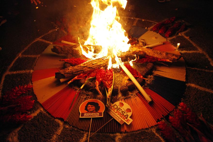 A small sign with a picture of murdered environmental activist Berta Caceres reads in Spanish, "We demand judgment and punishment," as people perform a ritual for Caceres outside the Supreme Court in Tegucigalpa, Honduras, Sunday, Sept. 16, 2018. The trial of eight men accused in her murder begins on Monday. (AP Photo/Fernando Antonio)