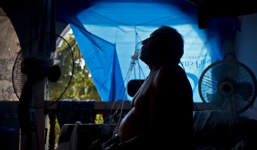 In this Sept. 9, 2018 photo, Gilberto Cosme Rodriguez takes one of his 10 a day asthma treatments to help him breathe, inside his home still covered with a tarp after FEMA assistance failed to cover the cost of fixing his roof that was torn off by last year's Hurricane Maria in Naranjito, Puerto Rico. Rodriguez, who has one working lung due to pulmonary fibrosis triggered by the use of chemicals when he worked in construction, said every morning he needs treatment to get out of bed. On a pension of $300 dollars, Rodriguez said it's barely enough to buy medicine. "I start the day like a dead person because of this lung problem," he said. (AP Photo/Ramon Espinosa)