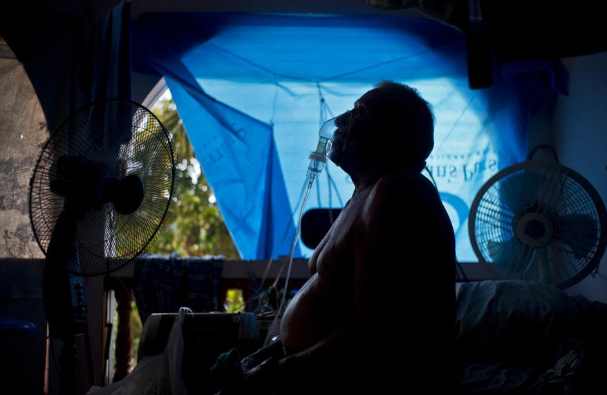 In this Sept. 9, 2018 photo, Gilberto Cosme Rodriguez takes one of his 10 a day asthma treatments to help him breathe, inside his home still covered with a tarp after FEMA assistance failed to cover the cost of fixing his roof that was torn off by last year's Hurricane Maria in Naranjito, Puerto Rico. Rodriguez, who has one working lung due to pulmonary fibrosis triggered by the use of chemicals when he worked in construction, said every morning he needs treatment to get out of bed. On a pension of $300 dollars, Rodriguez said it's barely enough to buy medicine. "I start the day like a dead person because of this lung problem," he said. (AP Photo/Ramon Espinosa)