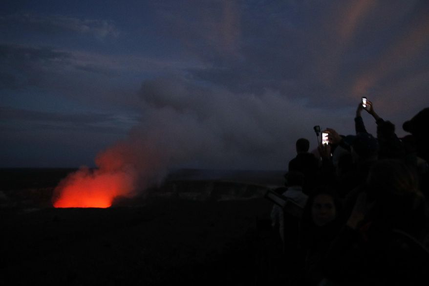 FILE - In this May, 9, 2018, file photo, visitors take pictures as Kilauea's summit crater glows red in Volcanoes National Park, Hawaii. The Hawaii Volcanoes National Park will reopen its main gates Saturday, Sept. 22, 2018, welcoming carloads of visitors eager to see Kilauea's new summit crater and the area where a longstanding lava lake once bubbled near the surface. The park has been closed for 135 days as volcanic activity caused explosive eruptions, earthquakes and the collapse of the famed Halemaumau crater. (AP Photo/Jae C. Hong, File)