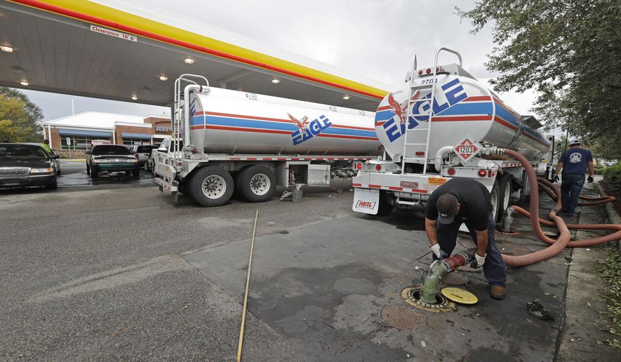 FILE- In this Sept. 17, 2018, file photo people wait in line as Travis Hall, right, and Brandon Deese, back, pump fuel from two tanker trucks at a convenience store in Wilmington, N.C. America's rediscovered prowess in oil production is shaking up old notions about the impact of higher crude prices on the U.S. economy. (AP Photo/Chuck Burton, File)