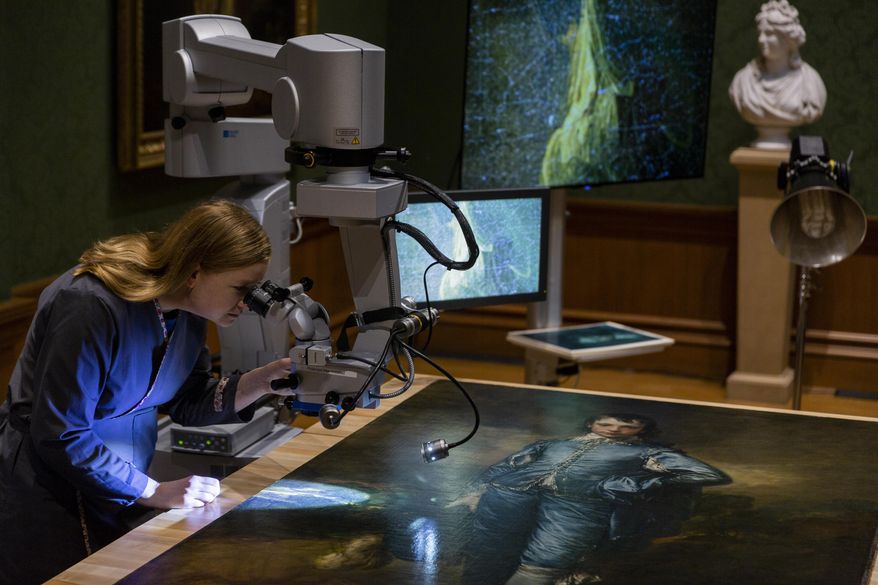 In this Thursday, Sept. 20, 2018, photo The Huntington's senior paintings conservator, Christina O'Connell, examines "The Blue Boy" painting, made around 1770 by the English painter Thomas Gainsborough (1727-1788), through a Haag-Streit surgical microscope at "Project Blue Boy" exhibit in the Thornton Portrait Gallery at The Huntington in San Marino, Calif. Beginning Saturday, Sept. 22, visitors to The Huntington Library, Art Collections and Botanical Gardens can see conservator Christina O’Connell repair Thomas Gainsborough’s priceless portrait of a boy dressed all in blue. (AP Photo/Damian Dovarganes)
