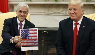 President Donald Trump, right, smiles as Chilean president Sebastian Pinera holds up a picture showing the Chilean flag at the center of the U.S. flag, in the Oval Office of the White House, Friday, Sept. 28, 2018, in Washington. (AP Photo/Alex Brandon)