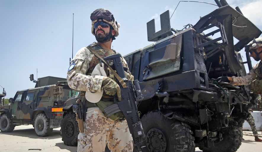 A member of the Italian military stands guard at the scene next to a damaged armored personnel carrier after an attack on a European Union military convoy in the capital Mogadishu, Somalia Monday, Oct. 1, 2018. (AP Photo/Farah Abdi Warsameh)