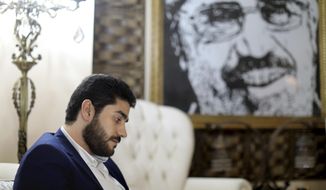 In this Sept. 30, 2018 photo, Abdullah Morsi, the youngest son of Egypt’s jailed former Islamist President Mohamed Morsi, sits in front of a framed image of his father that was printed on a flag during the 2013 Rabaah al-Adawiya sit-in, at his home in Cairo, Egypt. Abdullah is campaigning for more access to and better treatment for his father. The former president has been held for years in isolation and Abdullah says he is suffering from poor health. (AP Photo/Brian Rohan)