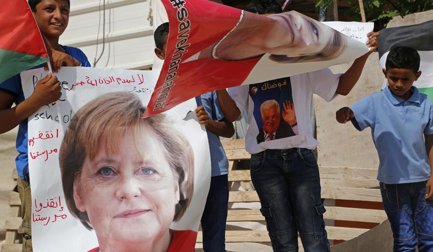 Bedouin children hold pictures of German Chancellor Angela Merkel ahead of her expected visit to Israel on Wednesday, in the West Bank Bedouin community of Khan al-Ahmar, Tuesday, Oct. 2, 2018. The children are pleading with Merkel to pressure Israel to halt demolition plans for the encampment of corrugated shacks outside an Israeli settlement east of Jerusalem. Arabic on the poster reads, "save Khan al-Ahmar" and "save our school." (AP Photo/Nasser Shiyoukhi)