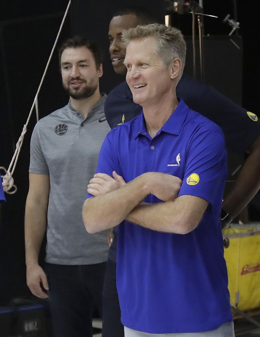 In this Sept. 24, 2018 photo, Golden State Warriors head coach Steve Kerr, foreground, waits to have photos taken with assistants Chris DeMarco, left, and Jarron Collins during media day at the NBA basketball team's practice facility in Oakland, Calif. Even the two-time defending NBA champions are seeking ways to reinvent themselves when it comes to preparation and practice routine. The Warriors are putting a greater emphasis on player development this training camp with a younger roster. (AP Photo/Jeff Chiu)
