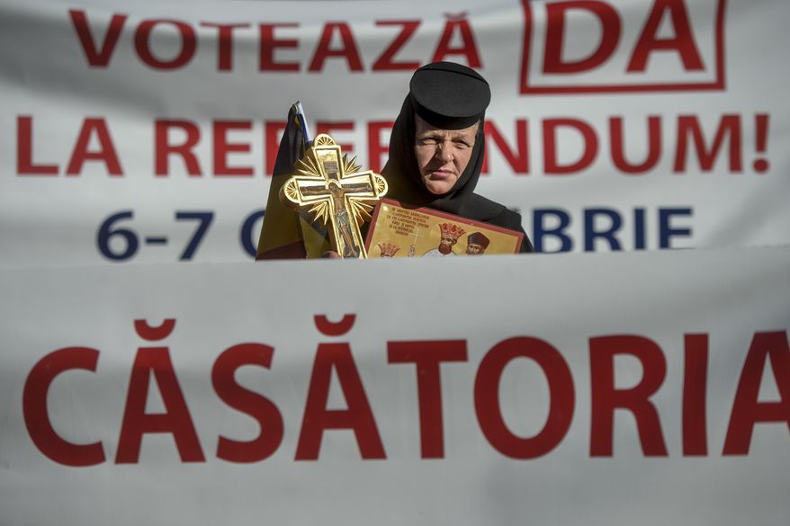 A nun holding a cross sits between banners that read in Romanian "Vote Yes on the Referendum! Marriage" during a rally in support of the traditional family, organised by the local church, in the small province town of Draganesti Olt, Romania, Thursday, Oct. 4, 2018. Romania will hold a referendum on October 6-7 after three million Romanians signed a petition demanding a constitutional amendment redefining marriage "as the union between a man and a woman", which is currently defined as a union between "spouses." (AP Photo/Andreea Alexandru)