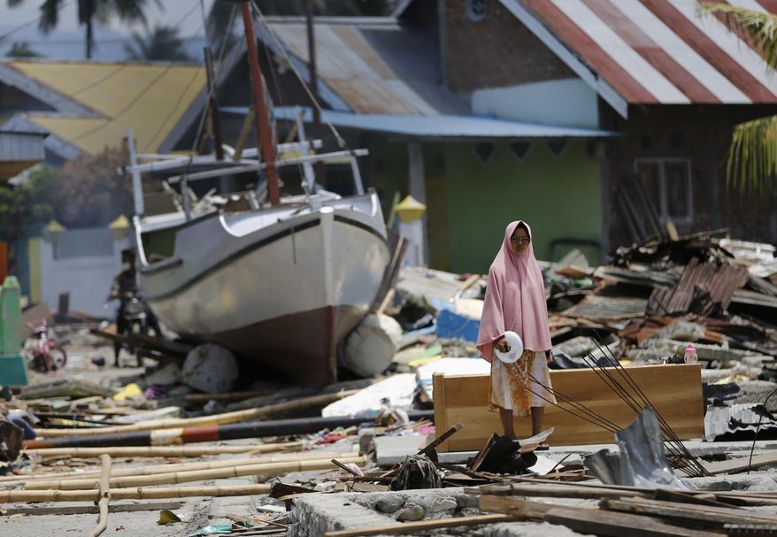 A woman stands in the rubble of houses as a boat swept ashore by tsunami rests on the ground in the background in Wani village on the outskirt of Palu, Central Sulawesi, Indonesia, Wednesday, Oct. 10, 2018. A 7.5 magnitude earthquake rocked Central Sulawesi province on Sept. 28, triggering a tsunami and mudslides that killed a large number of people and displaced tens of thousands of others. (AP Photo/Dita Alangkara)