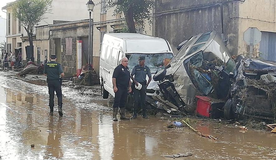 Police officers stand next to vehicles destroyed in Sant Llorenc, the town hardest hit by the downpours located 60 kilometers (40 miles) east of Mallorca's capital, Palma, Spain, on Wednesday, Oct. 10, 2018. At least five people died and five more remained missing on Wednesday after torrential rainstorms caused flash flooding in Spain's Mallorca island, authorities said. (AP Photo/Juan Pedro Martinez)