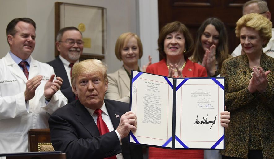 President Donald Trump holds up the 'Patient Right to Know Drug Prices Act' after signing it and the 'Know the Lowest Price Act of 2018,' during a ceremony in the Roosevelt Room of the White House in Washington, Wednesday, Oct. 10, 2018. These bills, which were sponsored by Sen. Susan Collins, R-Maine, in red, and Sen. Debbie Stabenow, D-Mich., right, help protect Medicare patients and those with private insurance from overpaying for prescription drugs by outlawing pharmacy "gag clauses." (AP Photo/Susan Walsh)