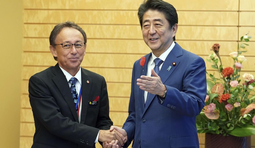 Okinawa Gov. Denny Tamaki, left, and Japanese Prime Minister Shinzo Abe shake hands during a meeting at Abe&#39;s office in Tokyo Friday, Oct. 12, 2018. Tamaki won the election for governor at the end of last month, becoming the first Amerasian to lead the southwestern Japanese islands. (AP Photo/Eugene Hoshiko, Pool)