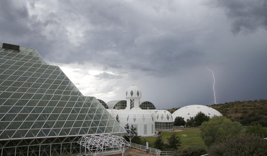 In this July 31, 2015 photo, several of the main buildings of the Biosphere 2 complex, including the tropical rainforest, left, the technosphere, middle, and the south lung, right, are shown as a thunderstorm moves past, in Oracle, Ariz. University of Arizona officials say that 25 years after that New Age-style experiment in the Arizona desert, the glass-covered greenhouse thrives as a singular site for researchers from around the world studying everything from the effects of the ocean’s acidification on coral to ways of ensuring food security. (AP Photo/Ross D. Franklin)