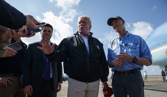 Gov. Rick Scott, R-Fla., right, looks on as President Donald Trump talks with reporters after arriving at Eglin Air Force Base to visit areas affected by Hurricane Michael, Monday, Oct. 15, 2018, in Eglin Air Force Base, Fla. (AP Photo/Evan Vucci)