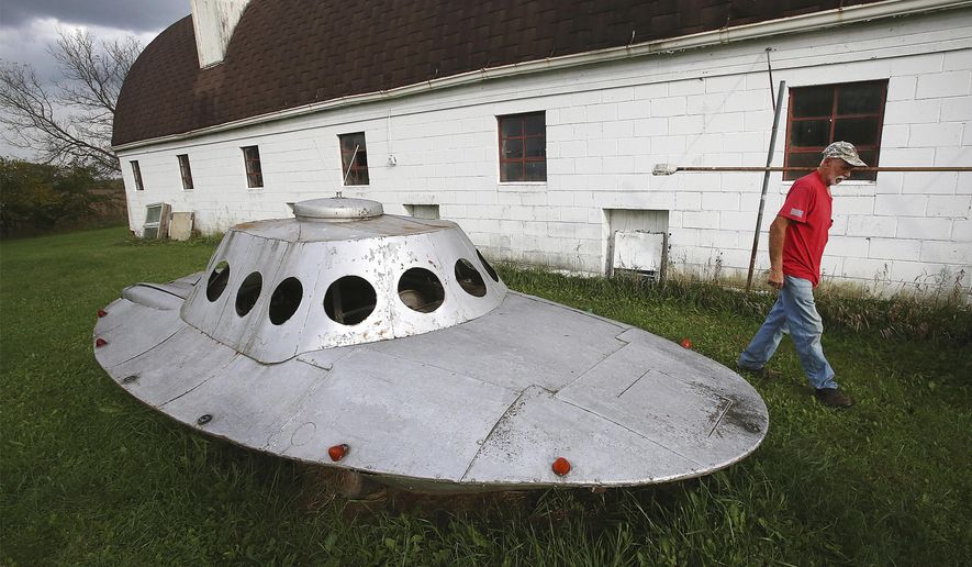 ADVANCE FOR USE SATURDAY, OCT. 20 - In this Tuesday, Oct. 9, 2018 photo, Bill Wolf, who crafted a spaceship onto the chassis of a 1976 Chevrolet Camaro in the 1980's, makes his way past the whimsical creation which resides on his property near Belleville, Wis. Comprised of metal panels salvaged from old washing machines and dryers, the drivable vehicle was made for the early days of the village's annual UFO Day gathering. (John Hart/Wisconsin State Journal via AP)