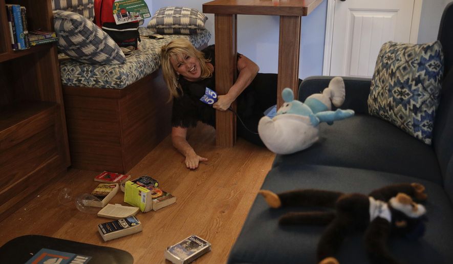 TV reporter Wendy Burch takes cover under a table in a Big Shaker simulating a 6.8 magnitude earthquake Thursday, Oct. 18, 2018, in Los Angeles. Millions of people around the world are practicing the basic earthquake safety skill of "drop, cover and hold on." Thursday marks the 10th anniversary of the "Great ShakeOut" earthquake drills that originated in Southern California. (AP Photo/Jae C. Hong)
