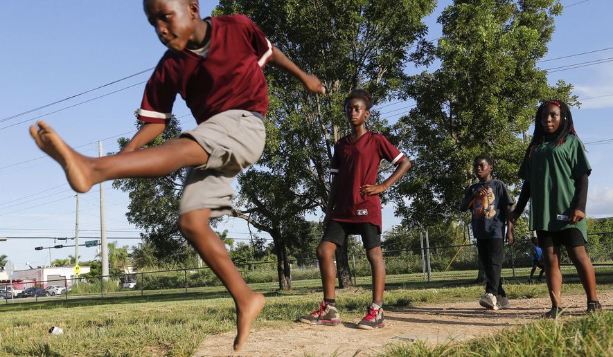 In this Aug. 23, 2018 photo, Kendall Conyers, 10, kicks a ball during a game of kickball while Leonna Mitchell, 10, Dedrick Melvin, 11, and Alicia Williams, 13, watch in Homestead, Fla. The kids are part of an the informal program called KICKS, or Keeping Inner City Kids Safe. It was organized by local parents to encourage children to exercise in a safe environment. (AP Photo/Ellis Rua)