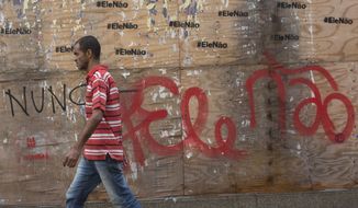 In this Oct. 17, 2018 photo, a man walks past graffiti that reads in Portuguese: &amp;quot;Not him&amp;quot; in Rio de Janeiro, Brazil.  Polls have consistently shown that both candidates for the presidency have the highest rates of rejection, defined as when a potential voter says he or she will not support a particular candidate under any circumstances. (AP Photo/Beatrice Christofaro)