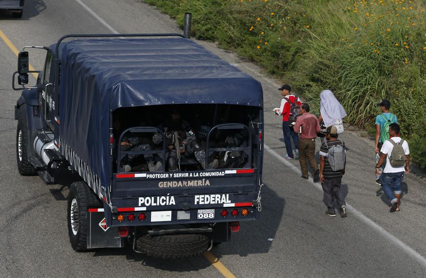 Mexican federal police drive away past Central Americans continuing on their journey, after police removed the blockade that had briefly halted a thousands-strong migrant caravan outside the town of Arriaga, Chiapas state, Mexico, Saturday, Oct. 27, 2018. Hundreds of Mexican federal officers carrying plastic shields had blocked the caravan from advancing toward the United States, after several thousand of the migrants turned down the chance to apply for refugee status and obtain a Mexican offer of benefits. (AP Photo/Rebecca Blackwell)