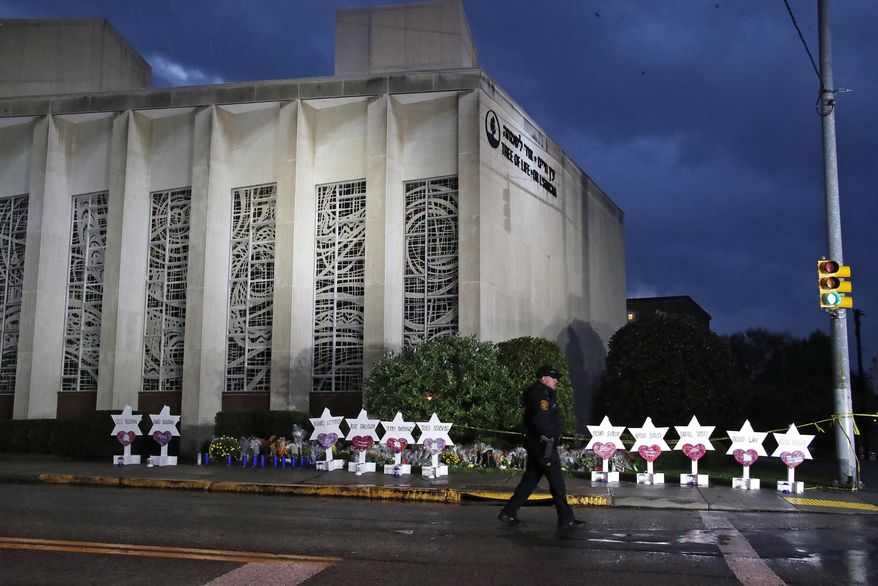 In this Oct. 28, 2018, file photo a Pittsburgh Police officer walks past the Tree of Life Synagogue and a memorial of flowers and stars in Pittsburgh in remembrance of those killed and injured when a shooter opened fire during services Saturday at the synagogue. (AP Photo/Gene J. Puskar, File)